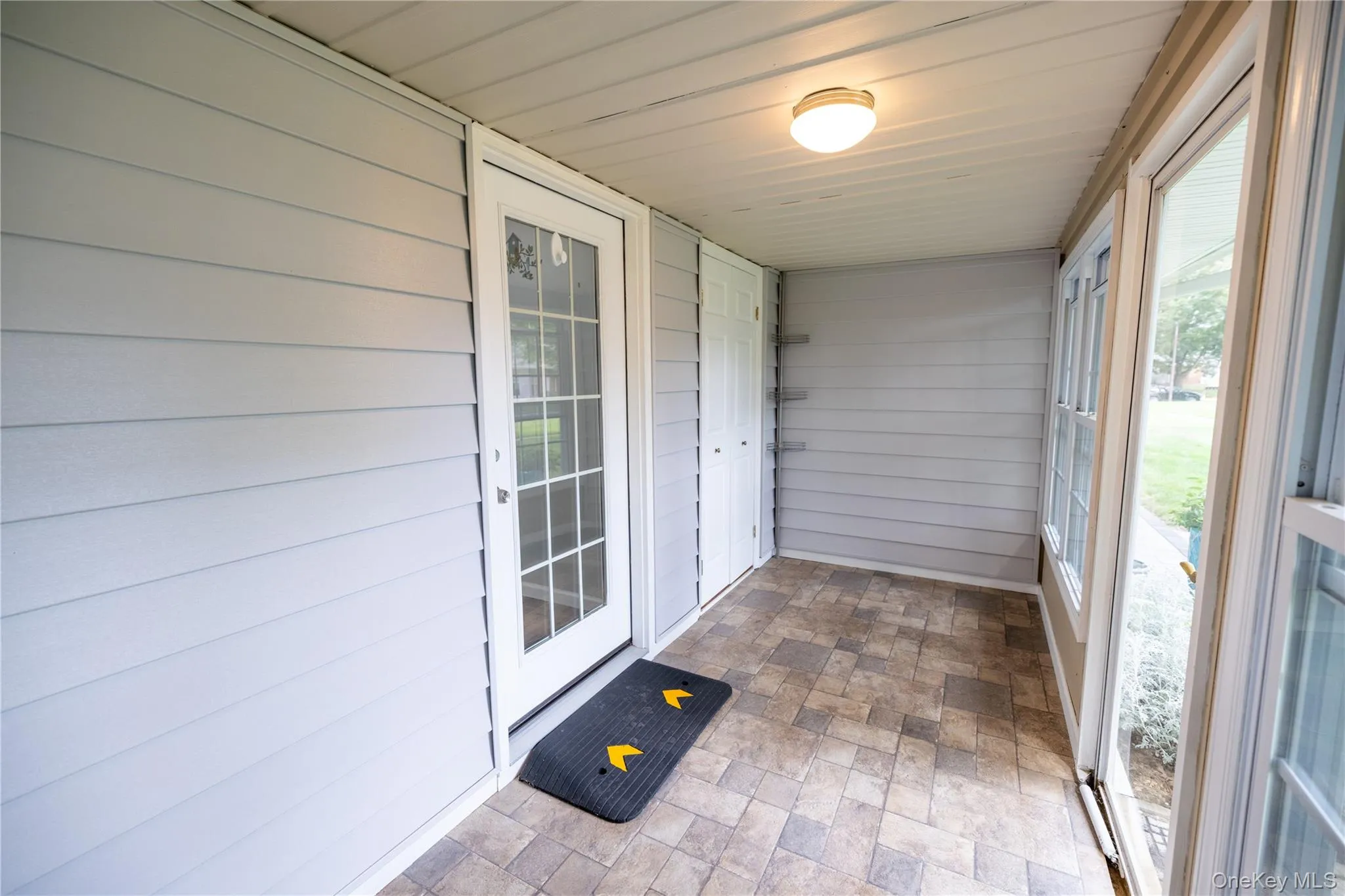 Screened porch with light gray siding, a full-lite door, a built-in storage closet, and patterned floor tiles Screened porch with light gray siding, a full-lite door, a built-in storage closet, and patterned floor tiles