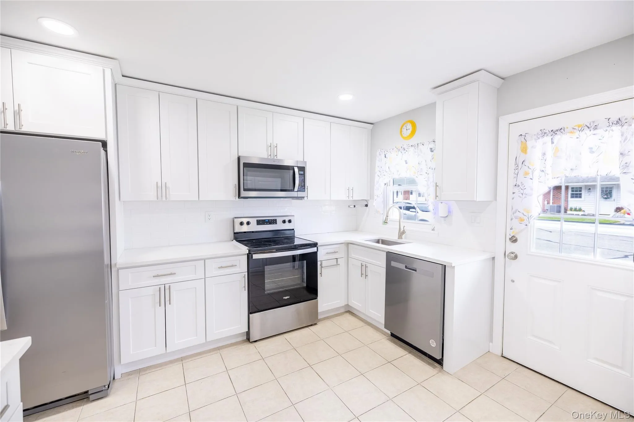 White cabinetry, stainless steel appliances, light-toned tiled flooring, white countertops, and a white subway tile backsplash White cabinetry, stainless steel appliances, light-toned tiled flooring, white countertops, and a white subway tile backsplash