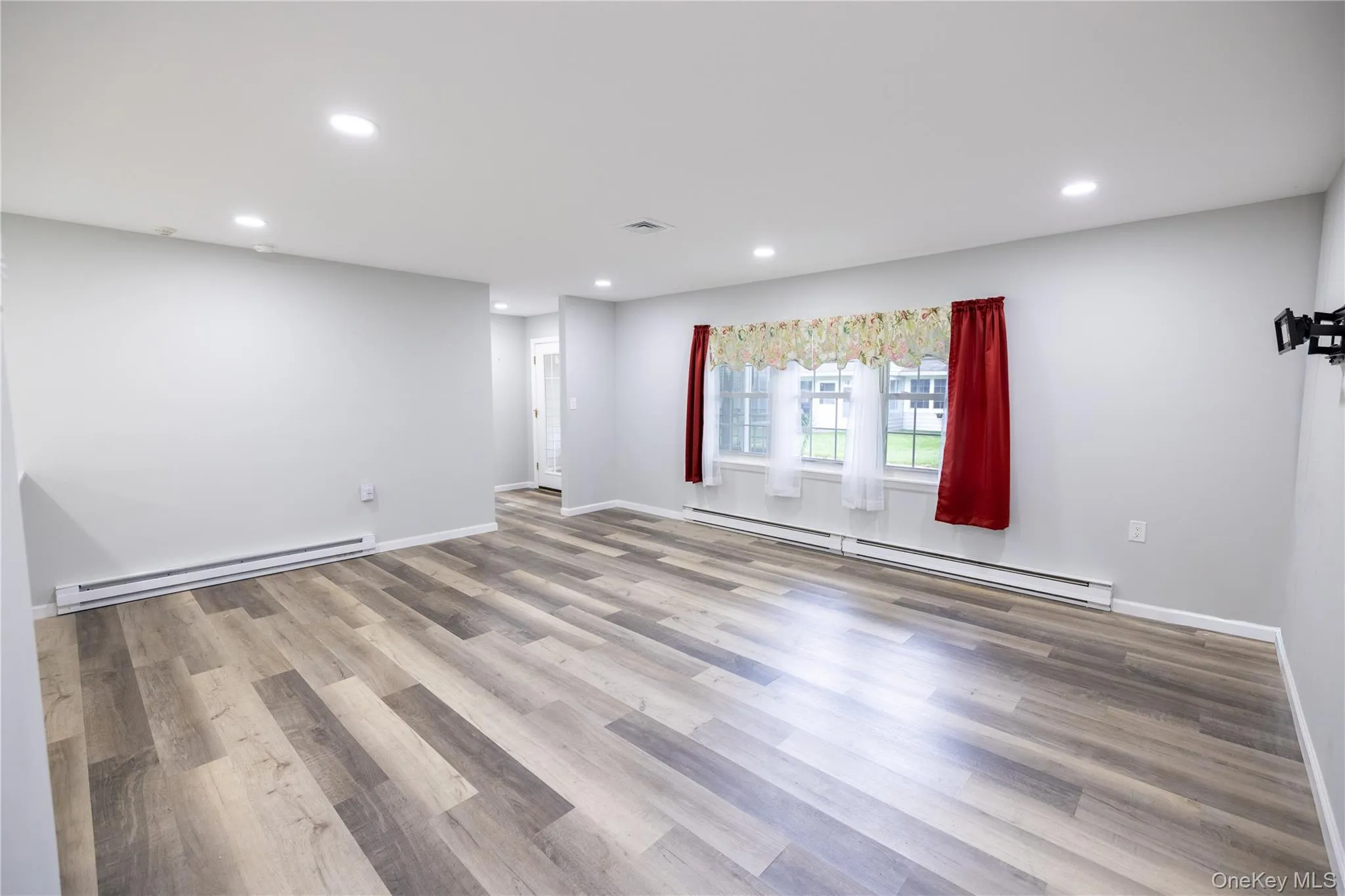 Spacious room featuring wood-finish flooring, recessed ceiling lighting, light gray wall paint, and multiple windows Spacious room featuring wood-finish flooring, recessed ceiling lighting, light gray wall paint, and multiple windows