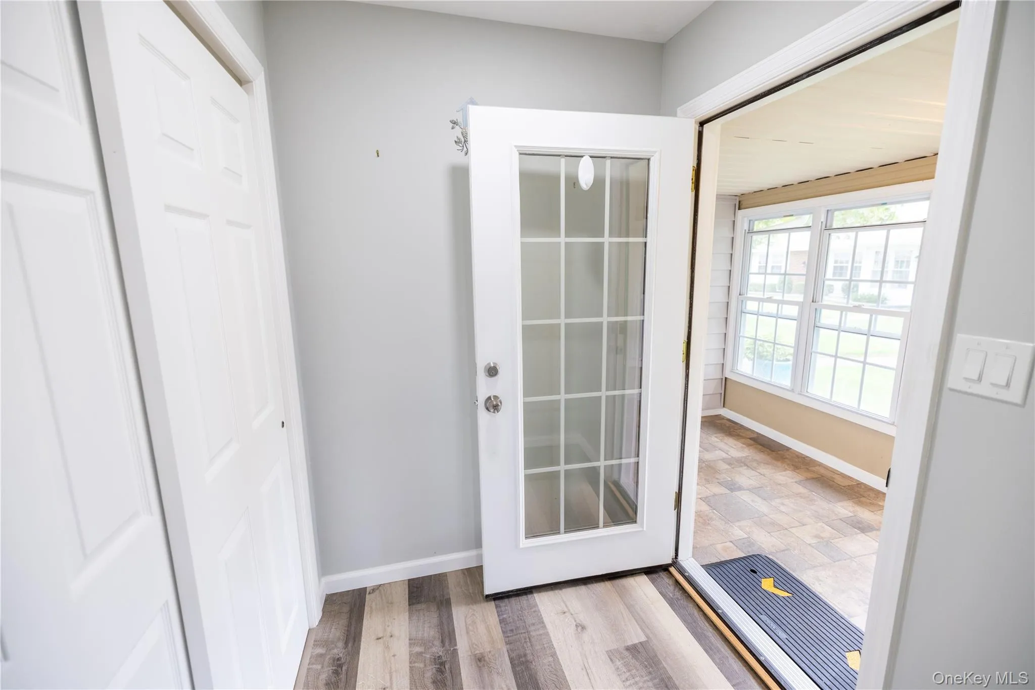 Wood-finish flooring, paneled white doors, light gray wall color, glass-paned door, and sunroom with multiple windows Wood-finish flooring, paneled white doors, light gray wall color, glass-paned door, and sunroom with multiple windows