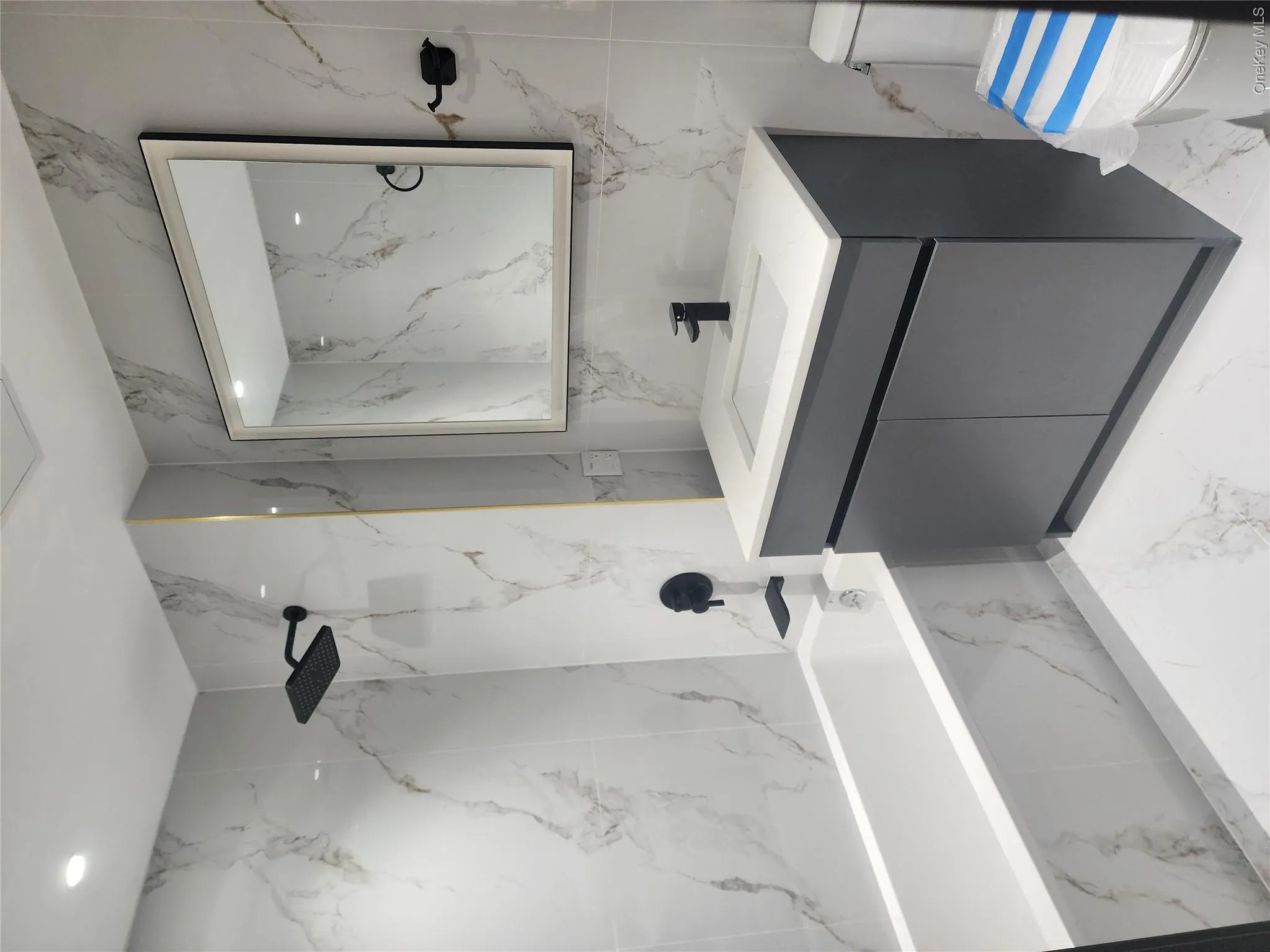 Bathroom featuring a white bathtub, vanity with a white countertop and dark gray cabinetry, matte black plumbing fixtures, and marble-look wall and floor tiling Bathroom featuring a white bathtub, vanity with a white countertop and dark gray cabinetry, matte black plumbing fixtures, and marble-look wall and floor tiling