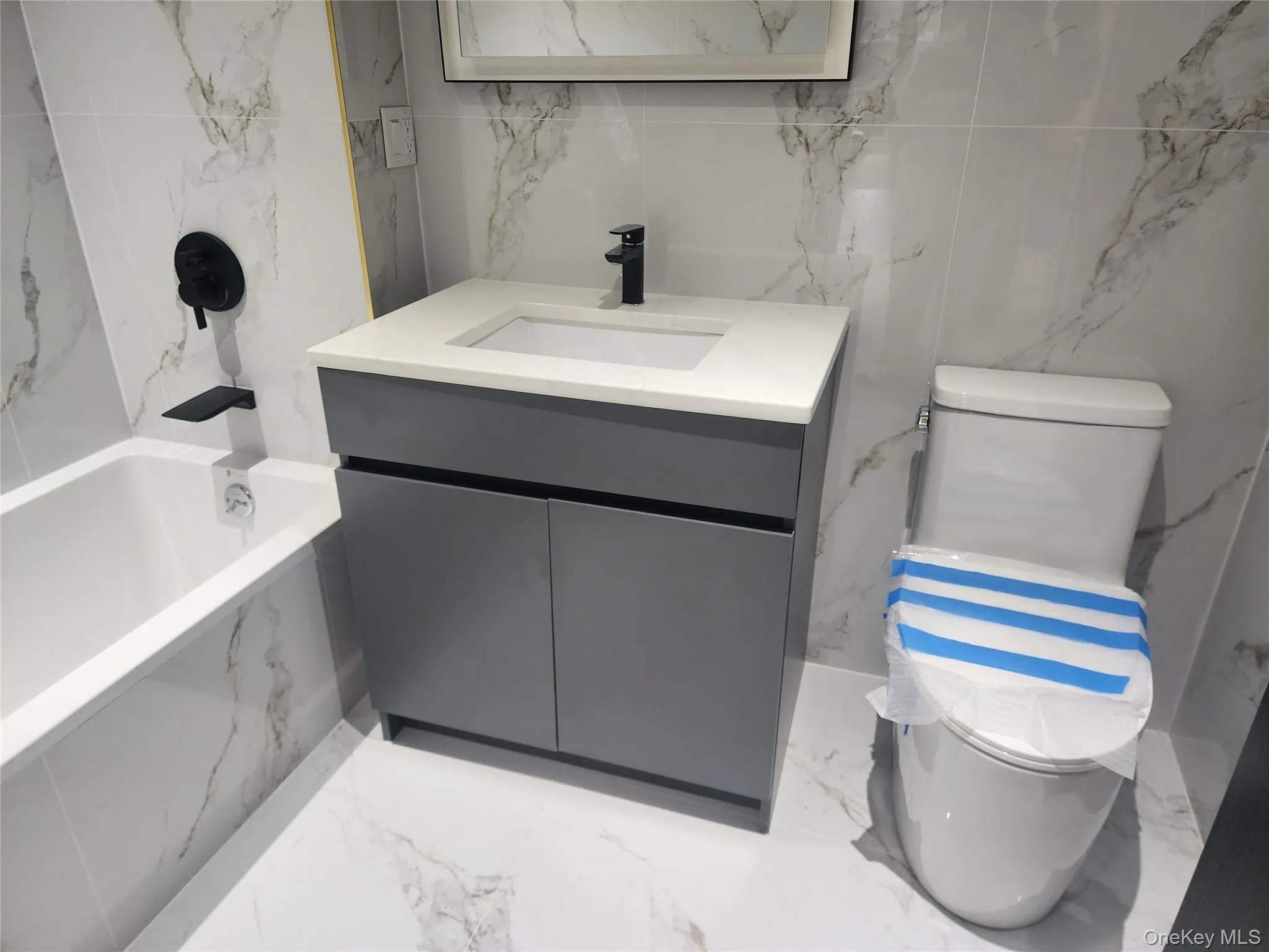 White marble-patterned tile flooring and wall surround with a gray vanity, white countertop, and black fixtures White marble-patterned tile flooring and wall surround with a gray vanity, white countertop, and black fixtures