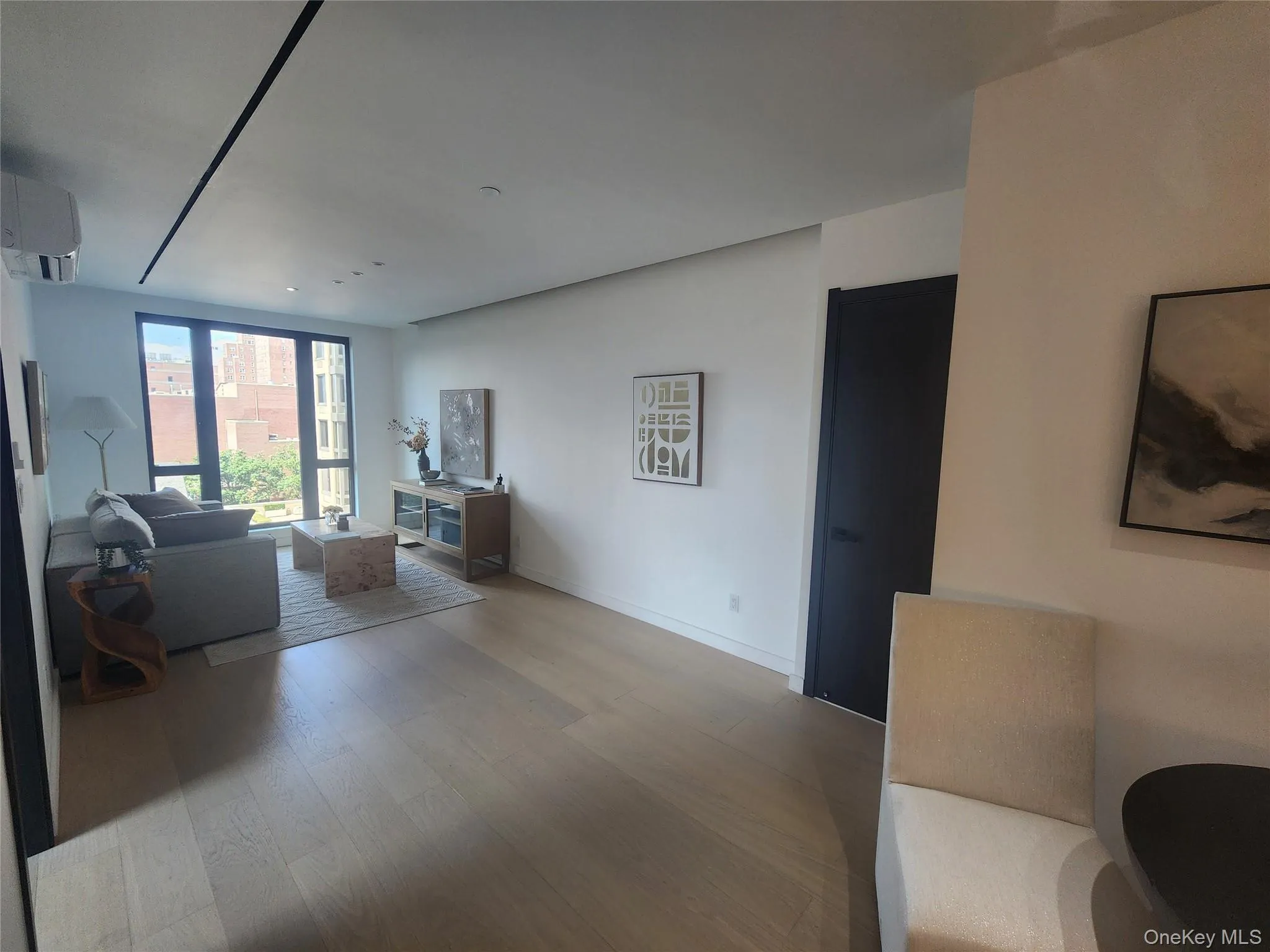 Expansive wood-finish flooring, full-height windows, a recessed lighting track, a built-in AC unit, and a contrasting dark interior door Expansive wood-finish flooring, full-height windows, a recessed lighting track, a built-in AC unit, and a contrasting dark interior door