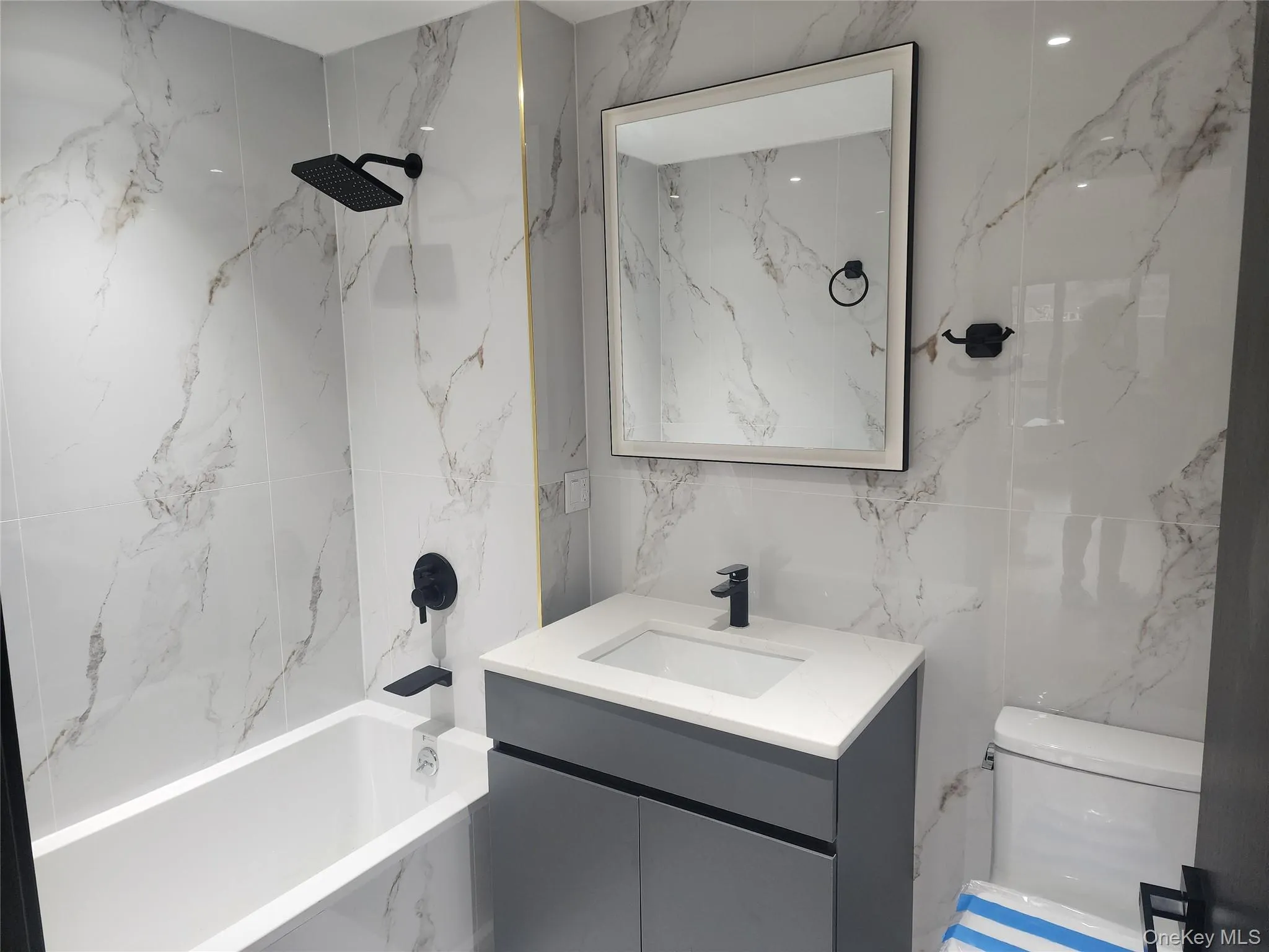 Full-height tiled shower surround, matte black fixtures, integrated bathtub, vanity with undermount sink, and wall-mounted mirror Full-height tiled shower surround, matte black fixtures, integrated bathtub, vanity with undermount sink, and wall-mounted mirror