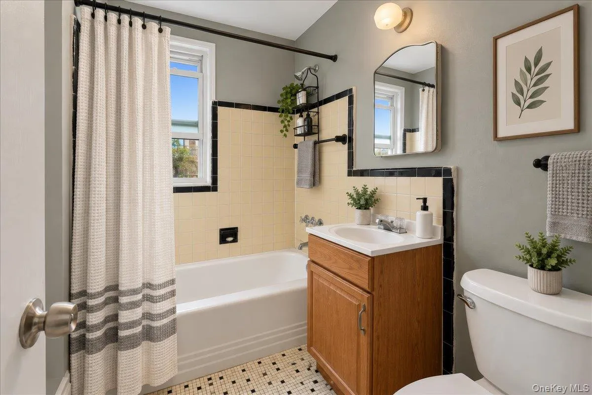 Bathroom featuring a white bathtub, ceramic wall tile with black trim, a wood-finish vanity with an integrated sink, and patterned floor tile Bathroom featuring a white bathtub, ceramic wall tile with black trim, a wood-finish vanity with an integrated sink, and patterned floor tile