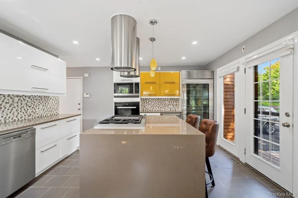 Modern kitchen featuring white and yellow cabinetry, a center island with an integrated cooktop, stainless steel appliances, and French doors Modern kitchen featuring white and yellow cabinetry, a center island with an integrated cooktop, stainless steel appliances, and French doors