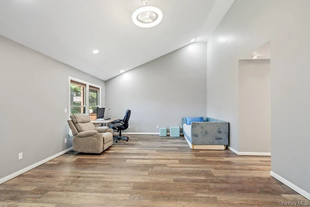 Vaulted ceiling with a flush-mount ceiling light and recessed lighting, wood-finish flooring, and a window with white trim Vaulted ceiling with a flush-mount ceiling light and recessed lighting, wood-finish flooring, and a window with white trim
