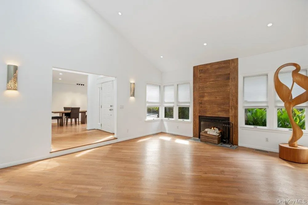 Vaulted ceiling, recessed lighting, wood-finish flooring, wood panel fireplace surround, multiple windows with white blinds Vaulted ceiling, recessed lighting, wood-finish flooring, wood panel fireplace surround, multiple windows with white blinds