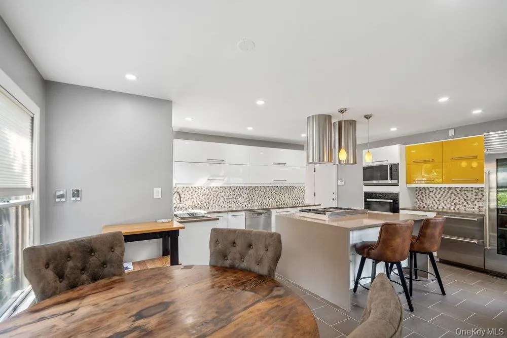 Modern kitchen featuring an island with integrated cooktop, white and yellow cabinetry, a mosaic tile backsplash, and stainless steel appliances Modern kitchen featuring an island with integrated cooktop, white and yellow cabinetry, a mosaic tile backsplash, and stainless steel appliances