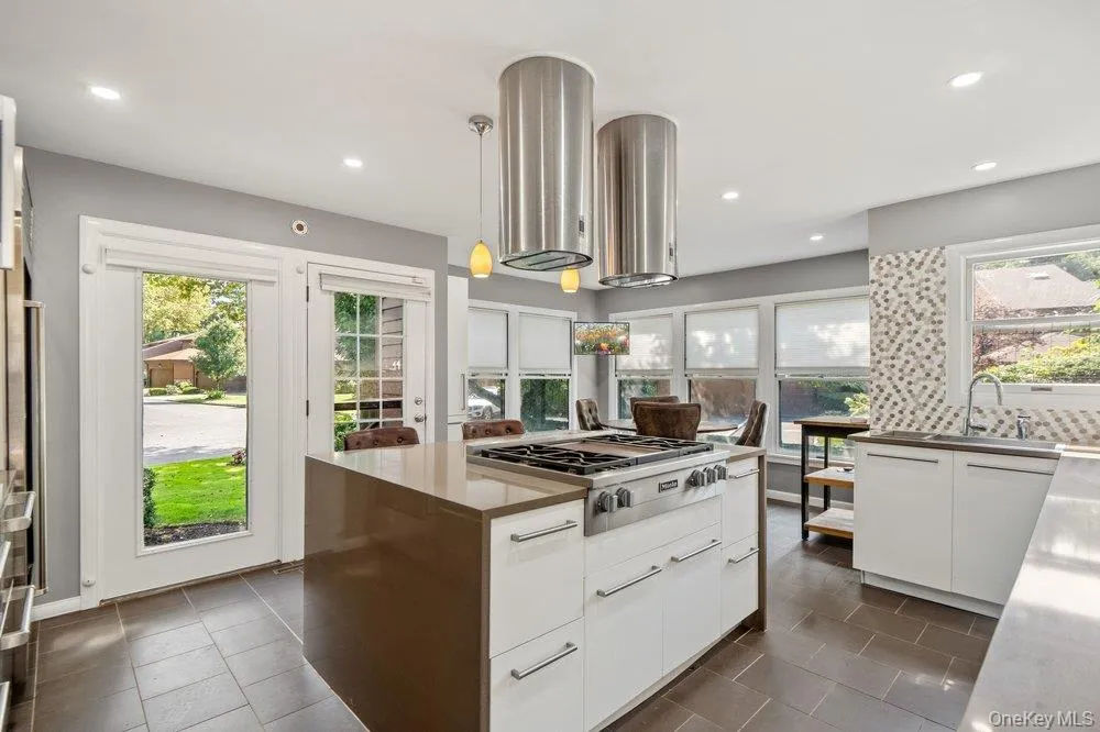 Kitchen featuring an expansive center island with a gas range, dual pendant lighting, stainless steel range hoods, and a mosaic tile backsplash Kitchen featuring an expansive center island with a gas range, dual pendant lighting, stainless steel range hoods, and a mosaic tile backsplash