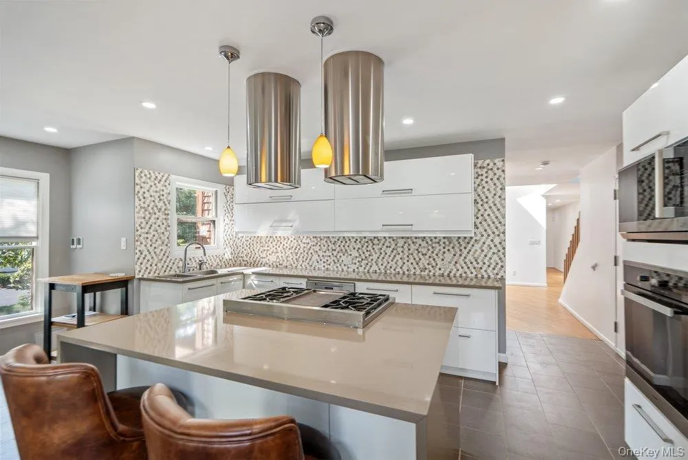 Kitchen featuring a large center island with an integrated cooktop, pendant lighting, white cabinetry, mosaic tile backsplash, and stainless steel appliances Kitchen featuring a large center island with an integrated cooktop, pendant lighting, white cabinetry, mosaic tile backsplash, and stainless steel appliances