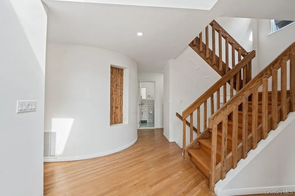 Hardwood flooring, natural wood staircase, recessed lighting, curved wall accent, and a built-in wood-paneled feature Hardwood flooring, natural wood staircase, recessed lighting, curved wall accent, and a built-in wood-paneled feature