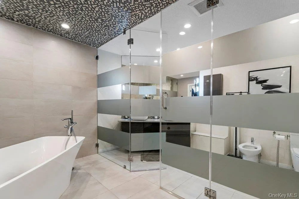 Freestanding soaking tub with floor-mounted faucet, glass-enclosed shower with frosted bands, mosaic tile ceiling, recessed lighting, and tile flooring Freestanding soaking tub with floor-mounted faucet, glass-enclosed shower with frosted bands, mosaic tile ceiling, recessed lighting, and tile flooring