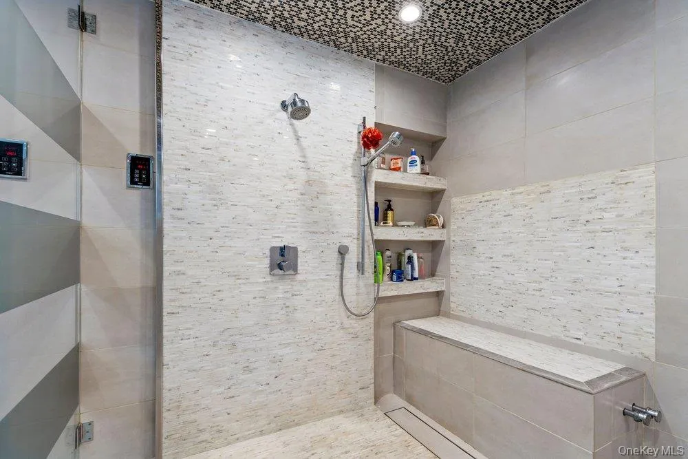 Shower with a built-in bench, integrated shelving, an overhead showerhead, a handheld sprayer, and a tiled ceiling Shower with a built-in bench, integrated shelving, an overhead showerhead, a handheld sprayer, and a tiled ceiling