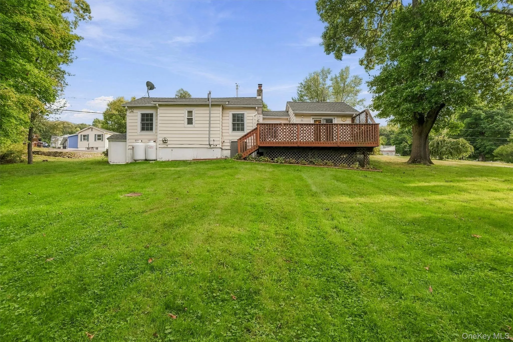 Expansive green lawn with a wood-tone deck featuring a lattice skirt Expansive green lawn with a wood-tone deck featuring a lattice skirt