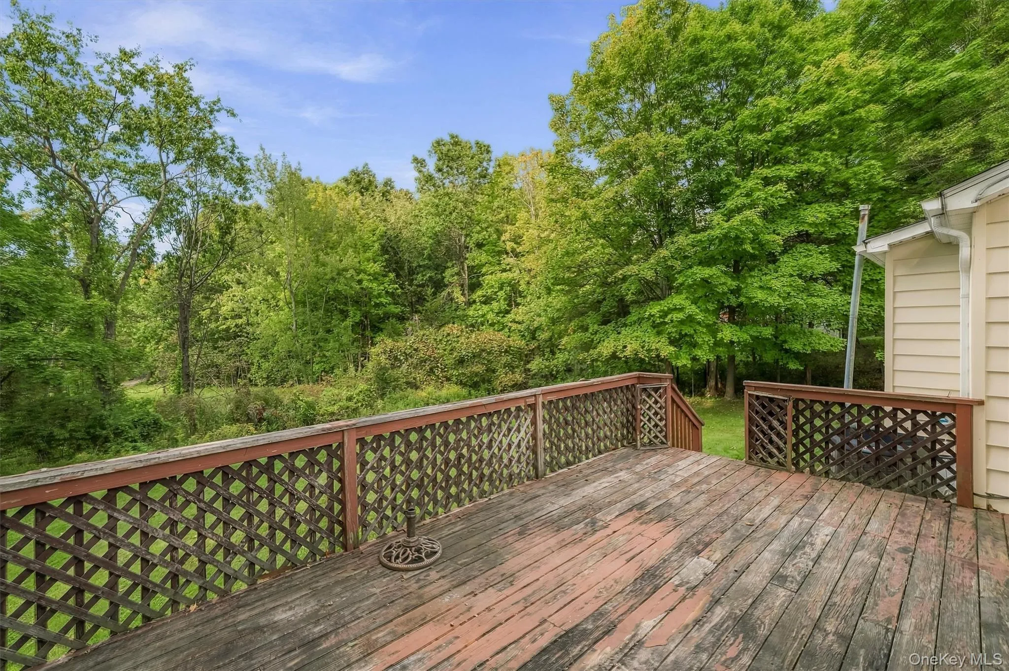 Expansive wood deck with lattice railing, surrounded by mature trees and greenery, featuring a natural landscape backdrop Expansive wood deck with lattice railing, surrounded by mature trees and greenery, featuring a natural landscape backdrop