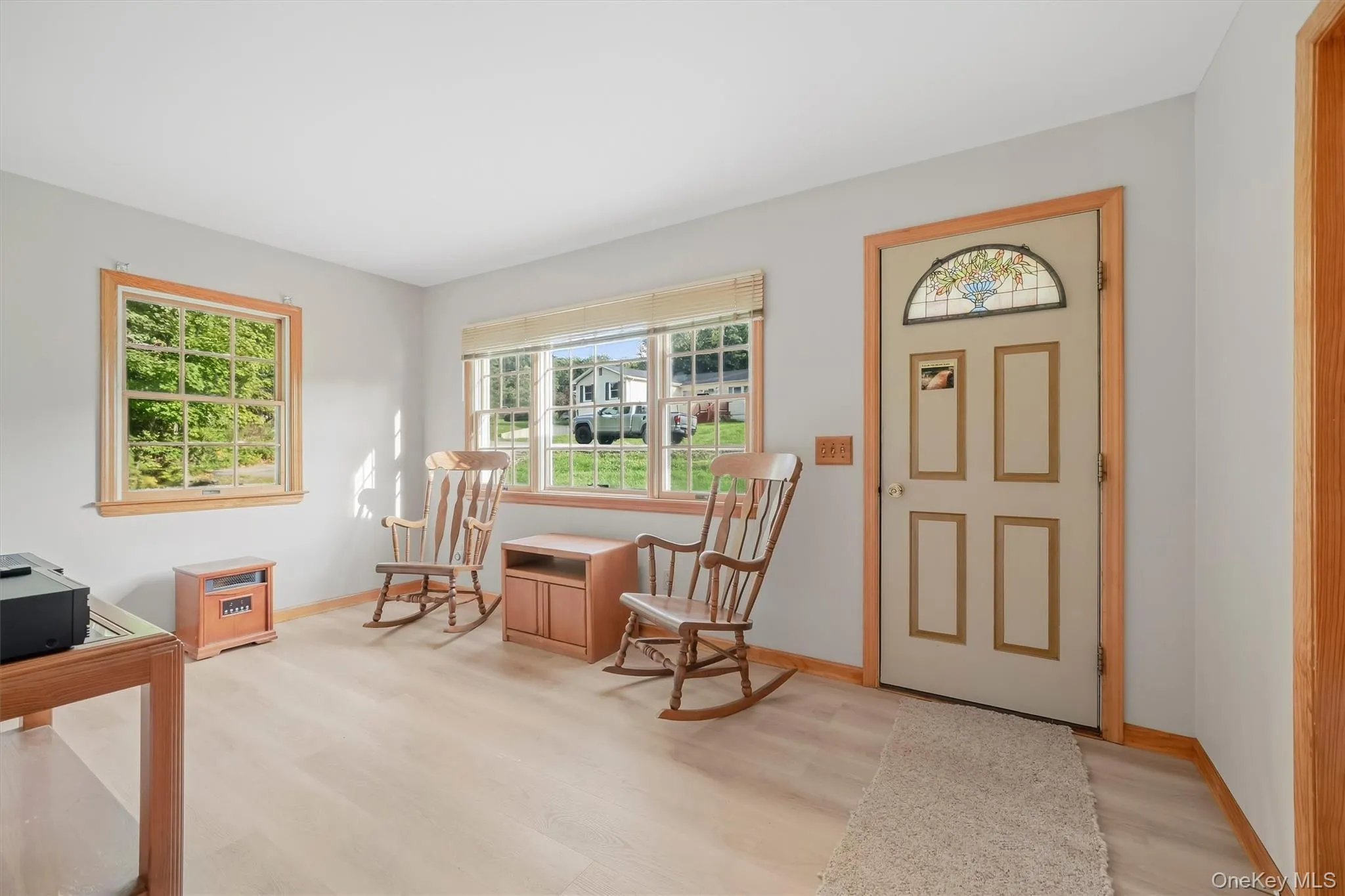 Light-toned wood-finish flooring, light grey wall paint, wood window trim, wood door trim, front door with decorative glass panel Light-toned wood-finish flooring, light grey wall paint, wood window trim, wood door trim, front door with decorative glass panel