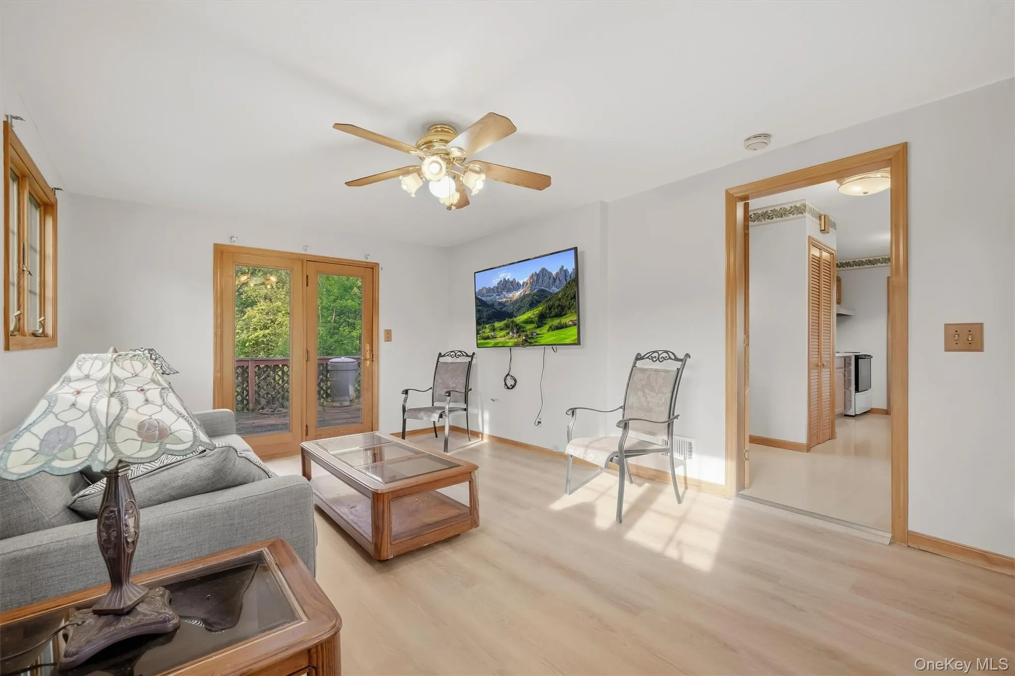 Light wood-finish flooring throughout, ceiling fan with integrated lighting, and wooden French doors leading to an exterior deck Light wood-finish flooring throughout, ceiling fan with integrated lighting, and wooden French doors leading to an exterior deck