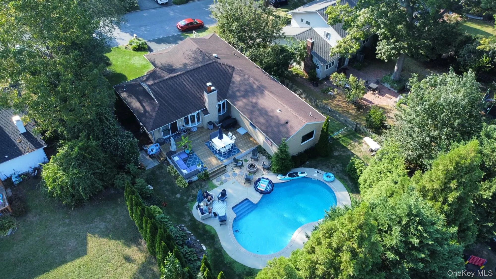 Expansive backyard featuring a custom-shaped swimming pool, a spacious wood deck, and mature perimeter landscaping Expansive backyard featuring a custom-shaped swimming pool, a spacious wood deck, and mature perimeter landscaping