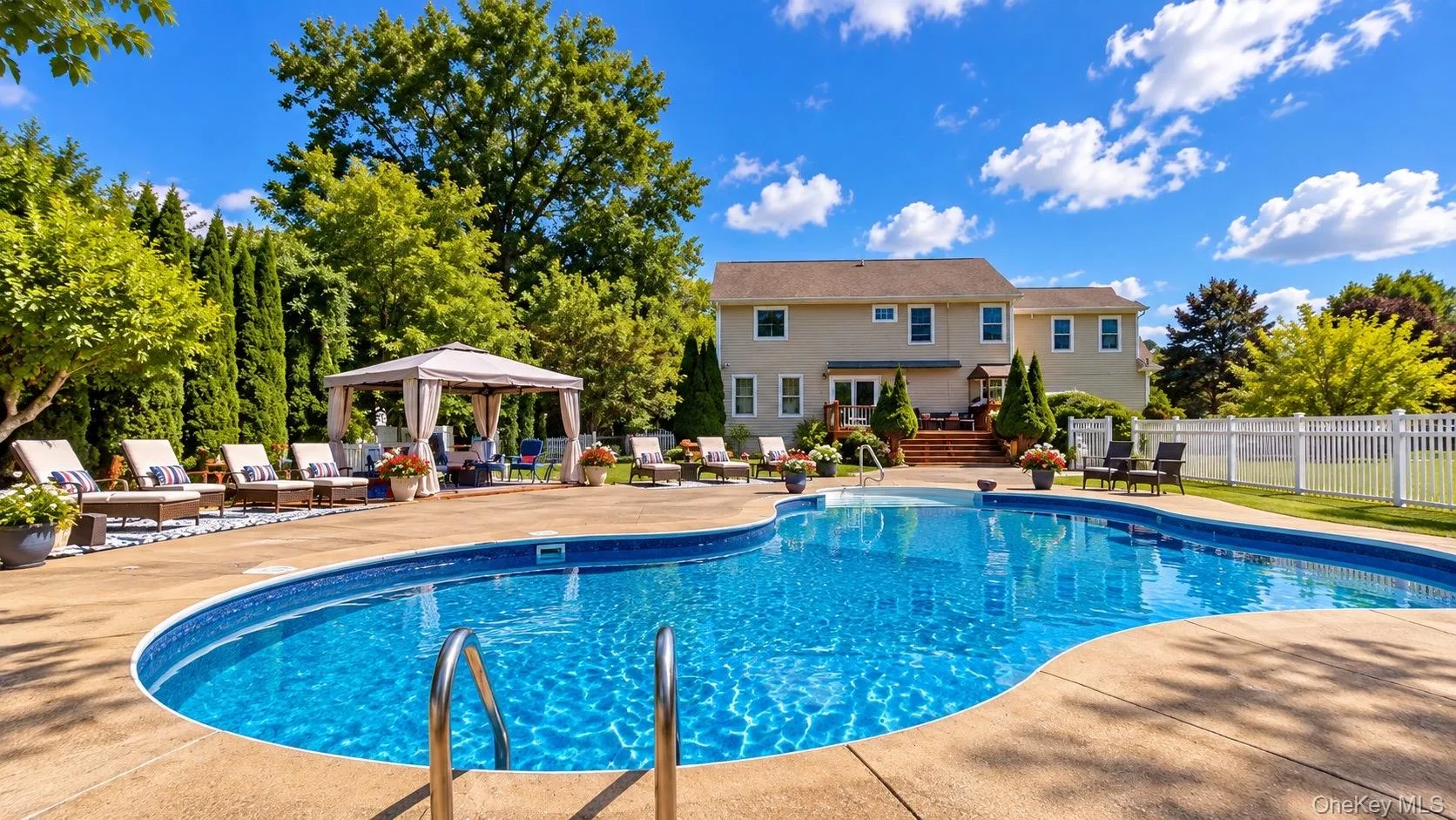 Expansive backyard featuring a large in-ground swimming pool, spacious concrete patio, a private gazebo, mature landscaping, and a white perimeter fence Expansive backyard featuring a large in-ground swimming pool, spacious concrete patio, a private gazebo, mature landscaping, and a white perimeter fence
