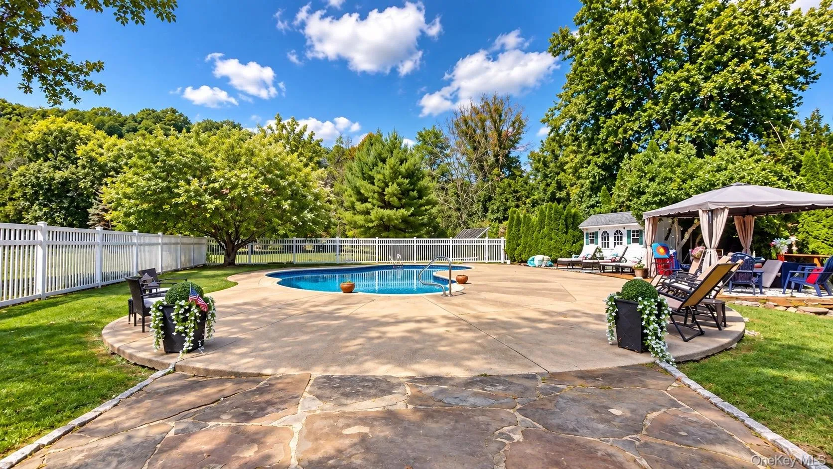 Expansive backyard featuring a built-in swimming pool, a full white picket fence, a stone paver patio, a gazebo, and a storage shed Expansive backyard featuring a built-in swimming pool, a full white picket fence, a stone paver patio, a gazebo, and a storage shed