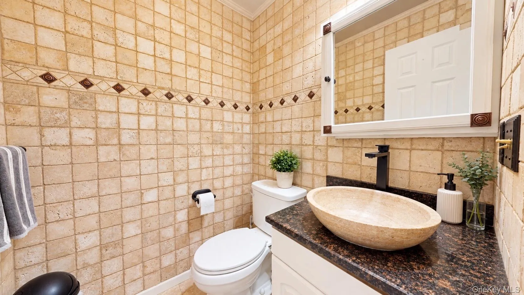 Full-height tile wall with decorative accent band, vessel sink, dark stone countertop, white vanity cabinetry, and a framed mirror Full-height tile wall with decorative accent band, vessel sink, dark stone countertop, white vanity cabinetry, and a framed mirror