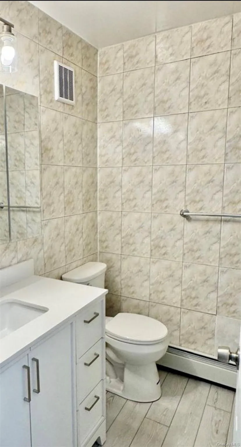 White vanity with an integrated sink, light-colored tile flooring, and fully tiled walls White vanity with an integrated sink, light-colored tile flooring, and fully tiled walls