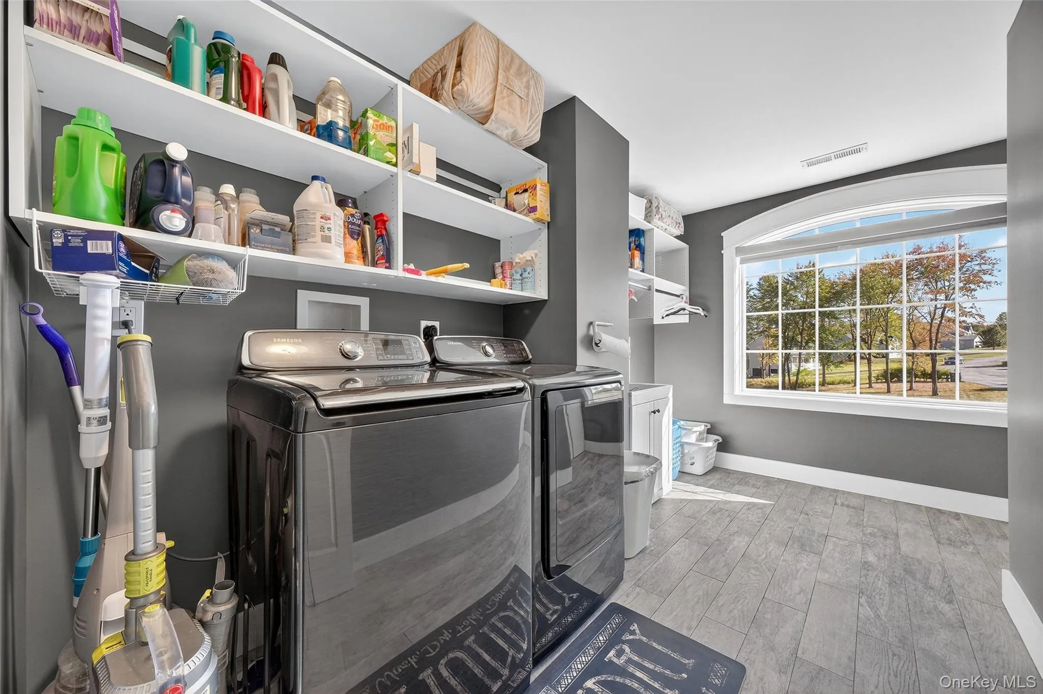 Second Floor Laundry room featuring wood-finish flooring, built-in shelving, an arched window, and a gray wall color Second Floor Laundry room featuring wood-finish flooring, built-in shelving, an arched window, and a gray wall color