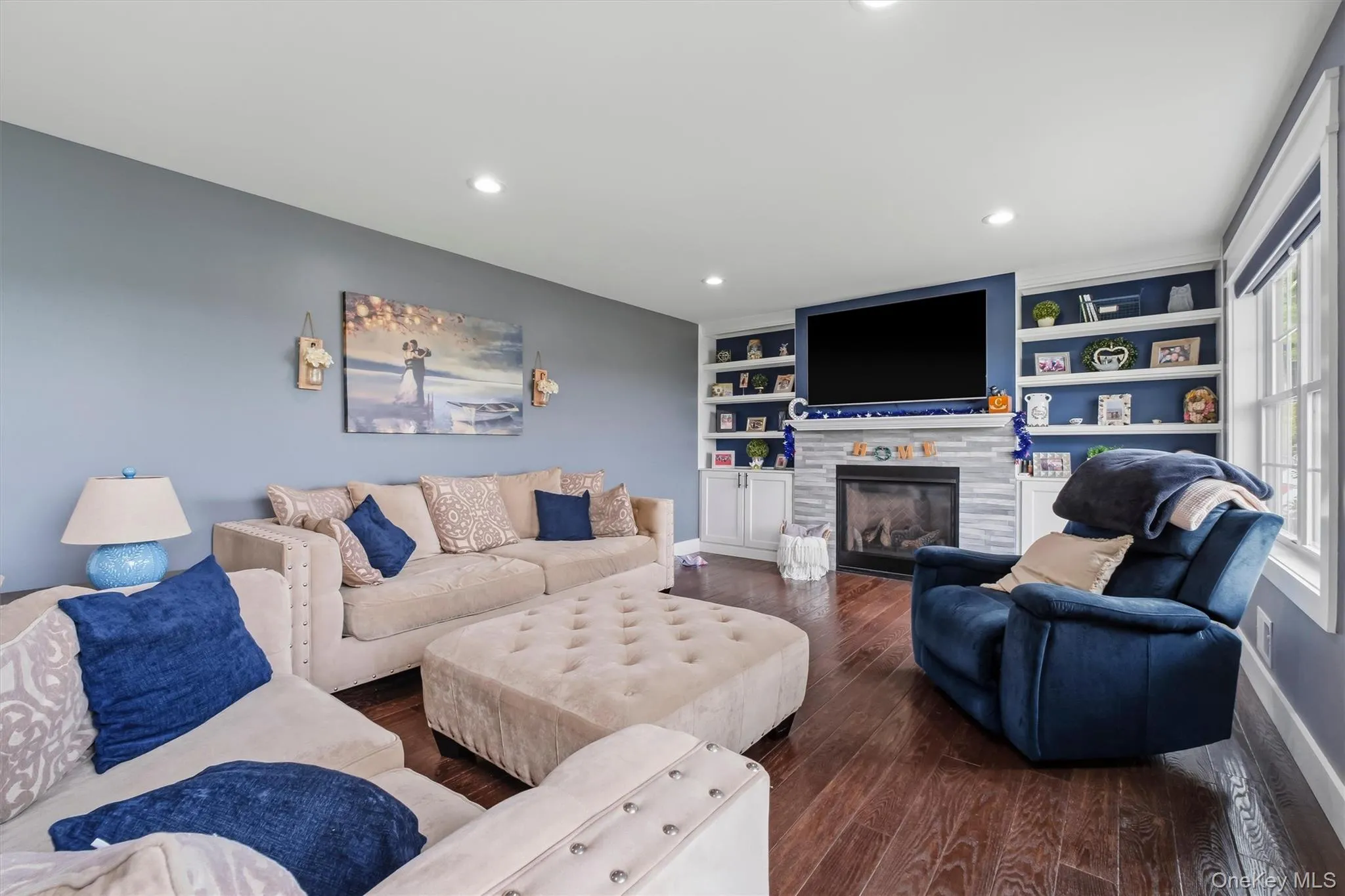 Hardwood flooring, recessed lighting, built-in shelving, stone-clad fireplace, and multiple windows Hardwood flooring, recessed lighting, built-in shelving, stone-clad fireplace, and multiple windows