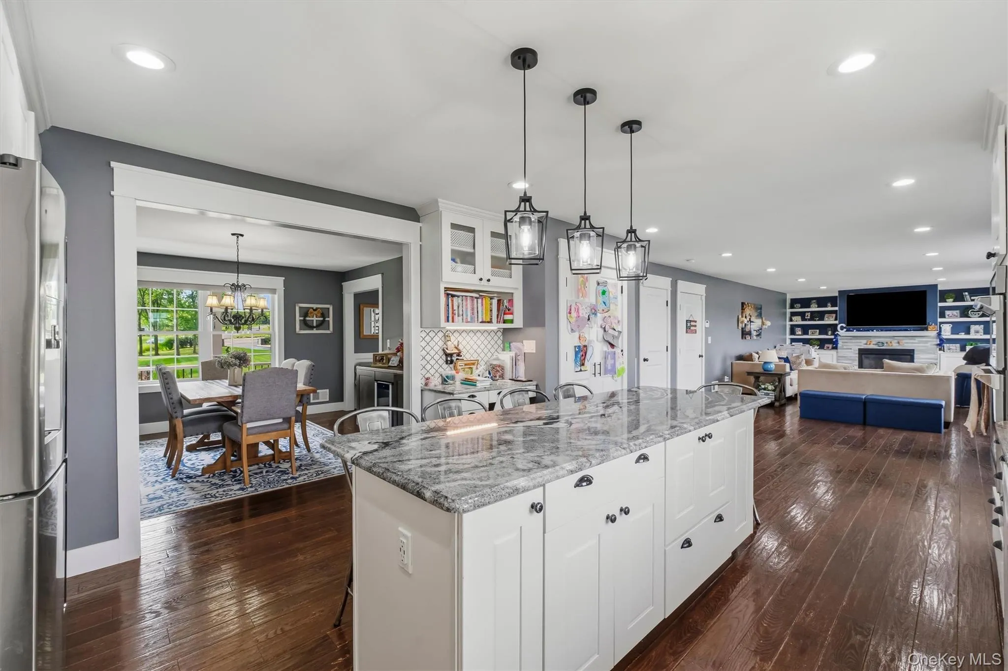 Spacious kitchen island with stone countertop, white cabinetry, dark wood-finish flooring, recessed lighting, and modern pendant lights Spacious kitchen island with stone countertop, white cabinetry, dark wood-finish flooring, recessed lighting, and modern pendant lights