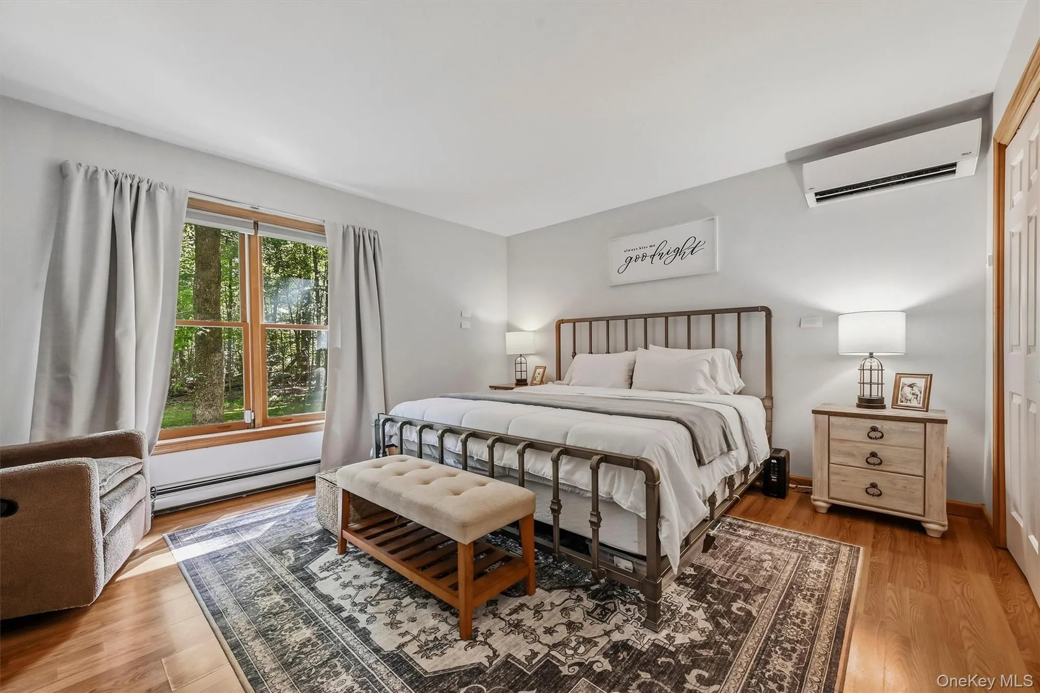 Hardwood flooring, window with exterior foliage, split-unit climate control, and neutral wall tones Hardwood flooring, window with exterior foliage, split-unit climate control, and neutral wall tones
