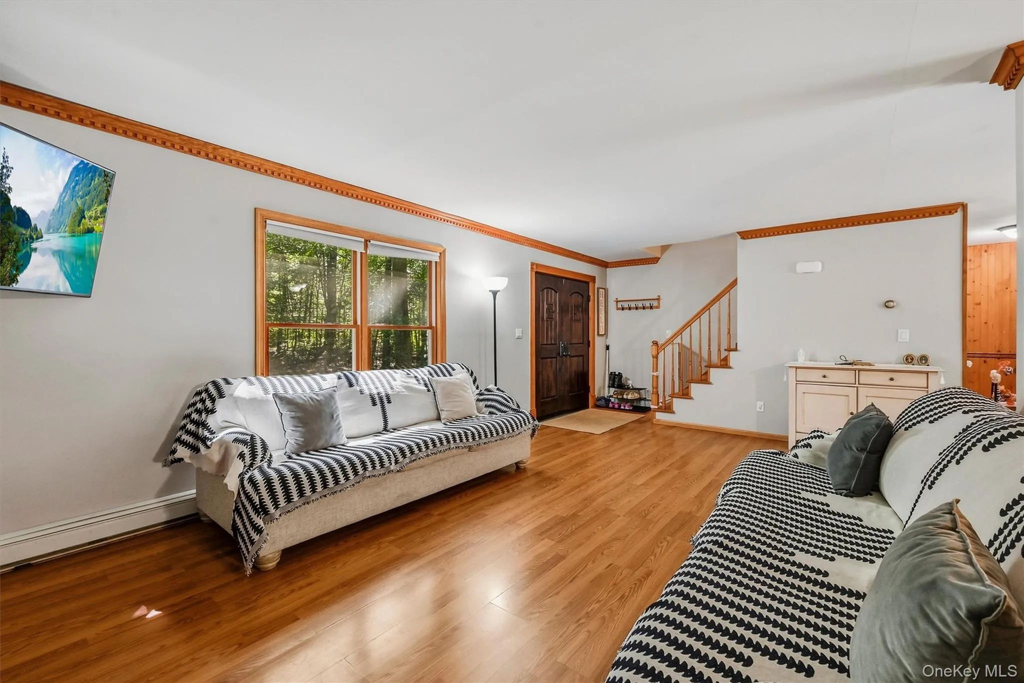 Wood-finish flooring, natural wood window trim, natural wood crown molding, a dark wood entry door, and a built-in staircase Wood-finish flooring, natural wood window trim, natural wood crown molding, a dark wood entry door, and a built-in staircase