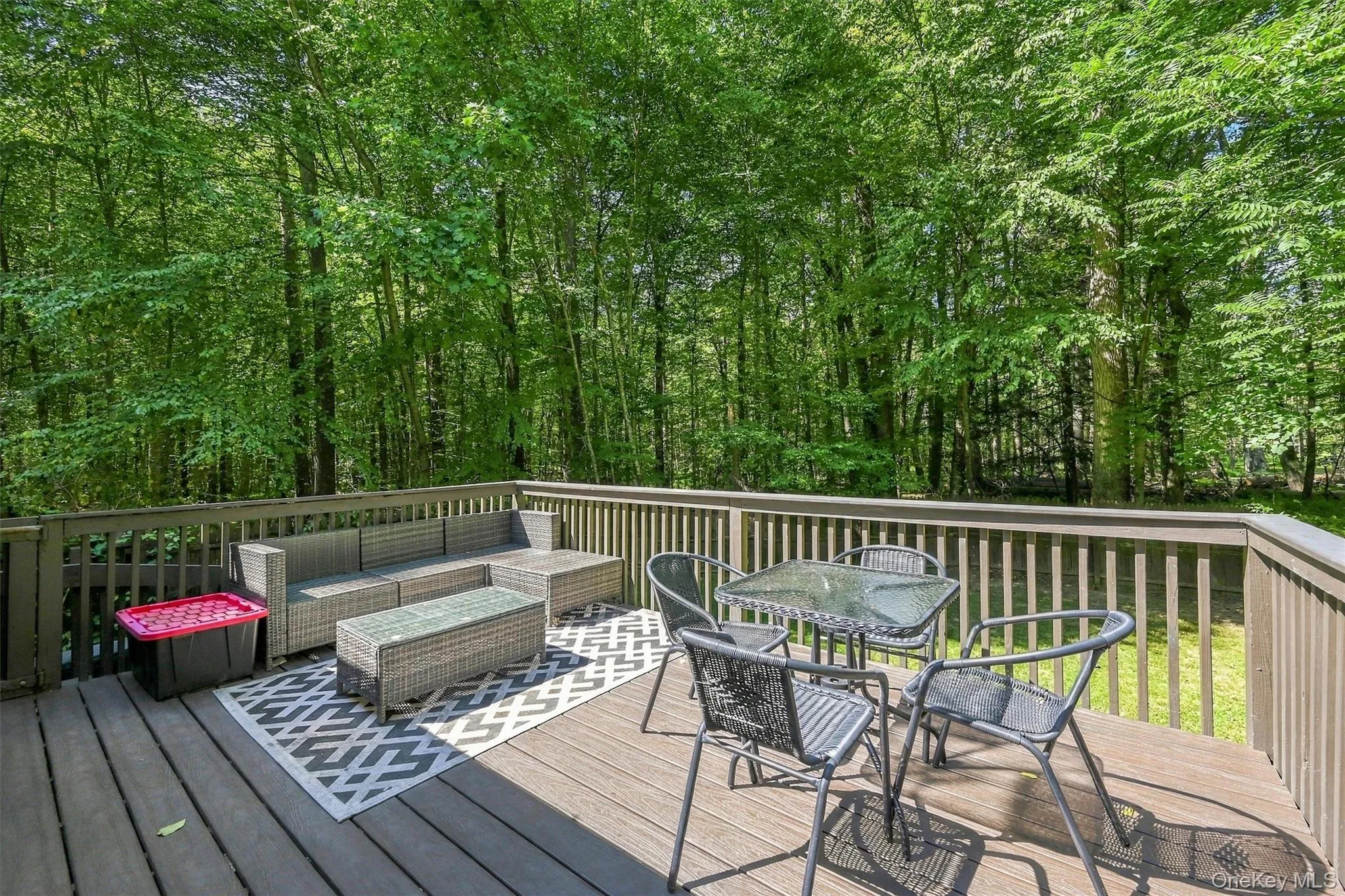 Expansive outdoor deck with wood-finish decking and perimeter railing, featuring a verdant tree line Expansive outdoor deck with wood-finish decking and perimeter railing, featuring a verdant tree line