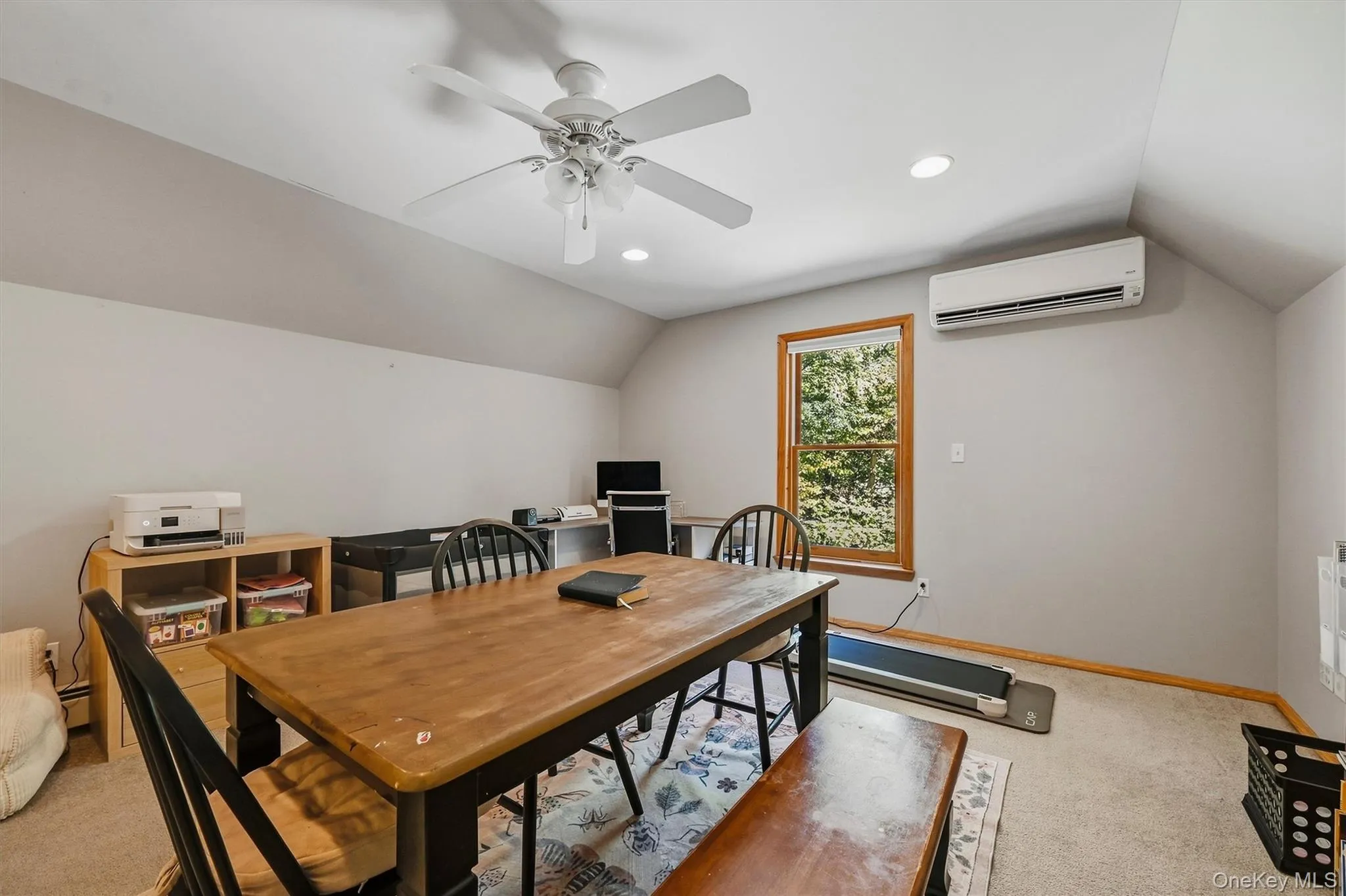 Sloped ceiling room featuring a window with wood trim, recessed lighting, a ceiling fan, and a wall-mounted climate control unit Sloped ceiling room featuring a window with wood trim, recessed lighting, a ceiling fan, and a wall-mounted climate control unit