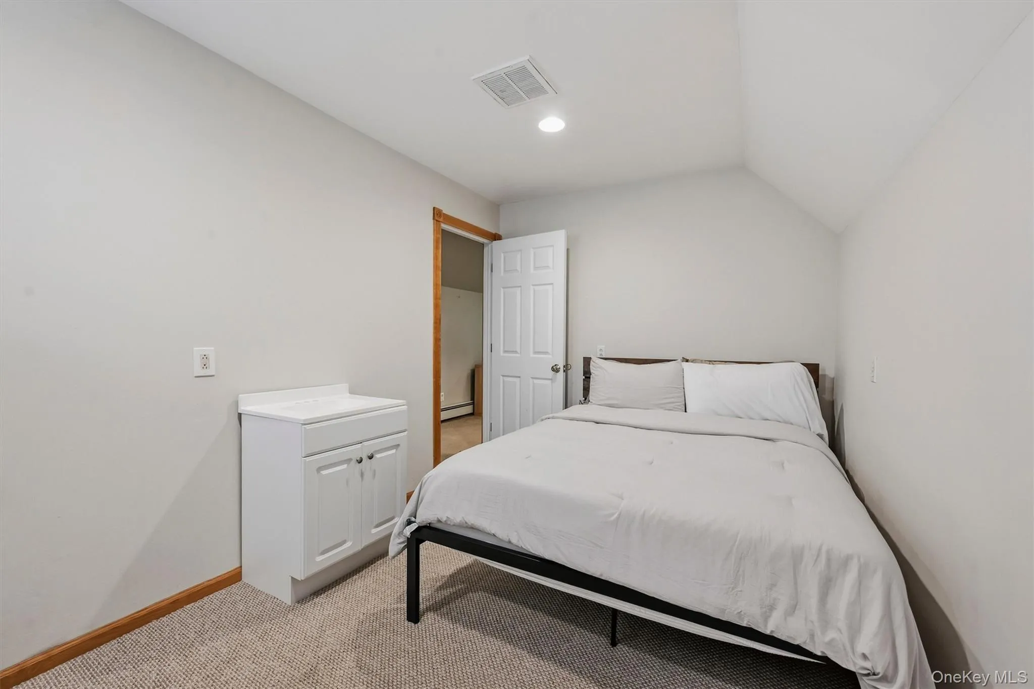 White vanity with a rectangular sink and white countertop, vaulted ceiling, recessed lighting, and light-colored carpeting White vanity with a rectangular sink and white countertop, vaulted ceiling, recessed lighting, and light-colored carpeting