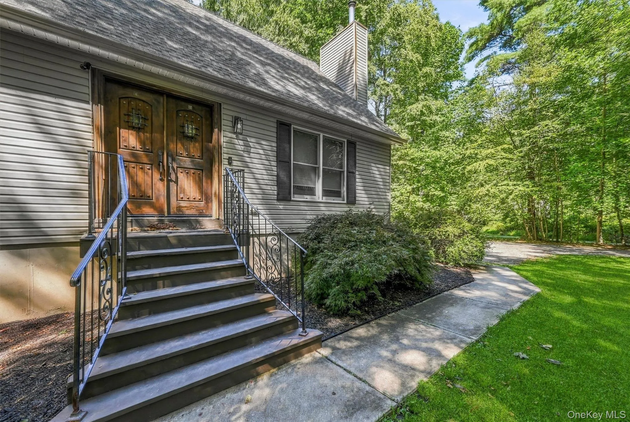 Exterior featuring siding, a prominent chimney, an ornate double-door entry, a stone staircase with wrought iron railings, and a concrete pathway Exterior featuring siding, a prominent chimney, an ornate double-door entry, a stone staircase with wrought iron railings, and a concrete pathway