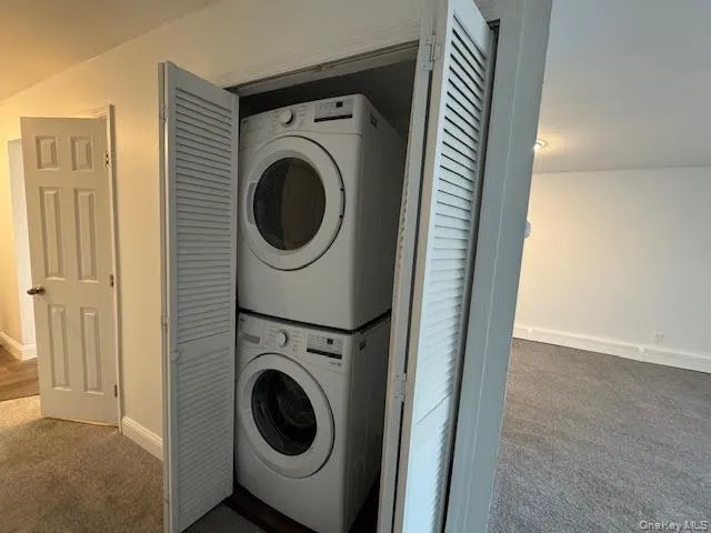 Laundry room featuring dark colored carpet and estacked washer and dryer Laundry room featuring dark colored carpet and estacked washer and dryer