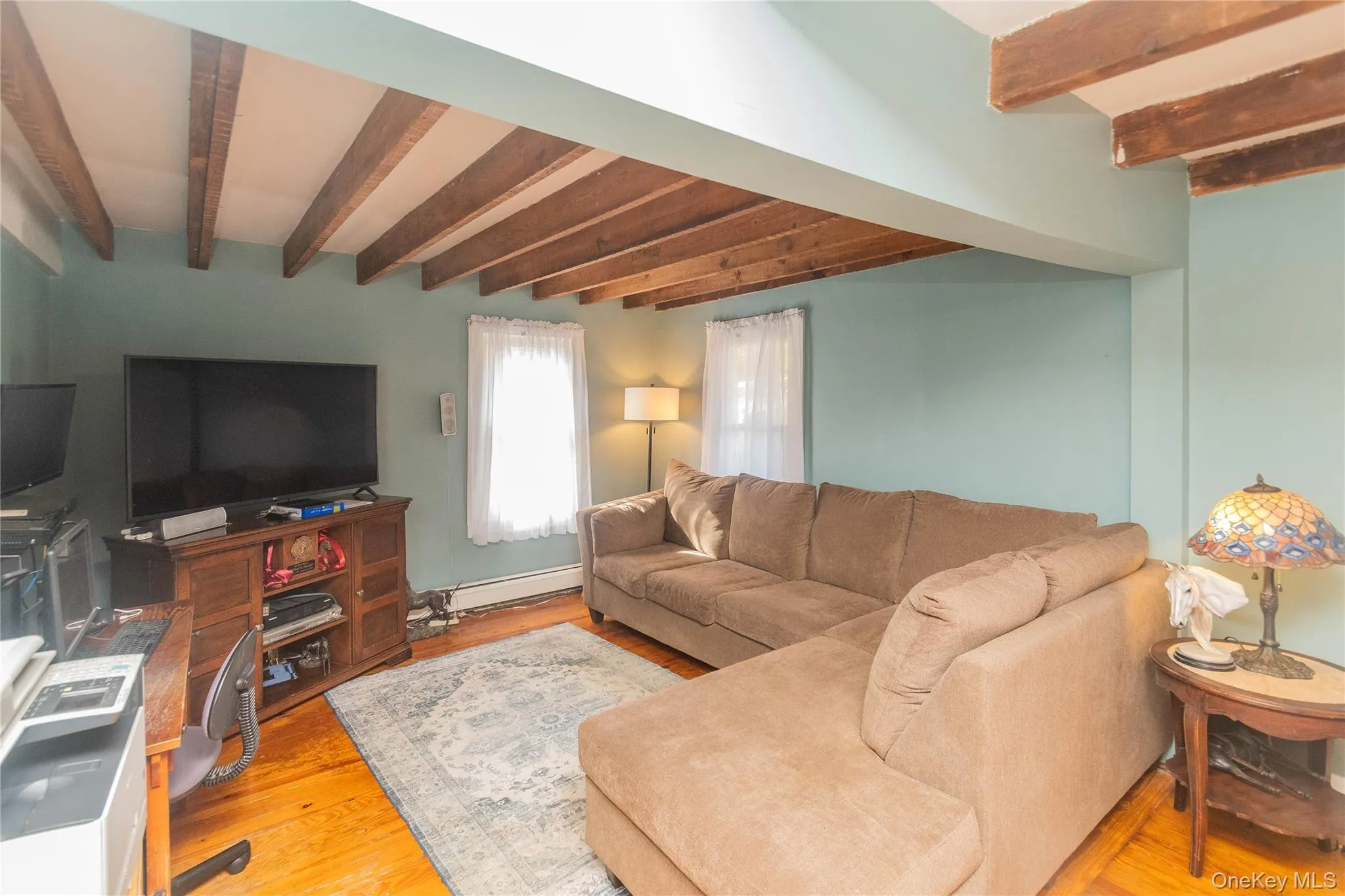 Living area featuring beamed ceiling, light wood-type flooring, and a baseboard radiator Living area featuring beamed ceiling, light wood-type flooring, and a baseboard radiator