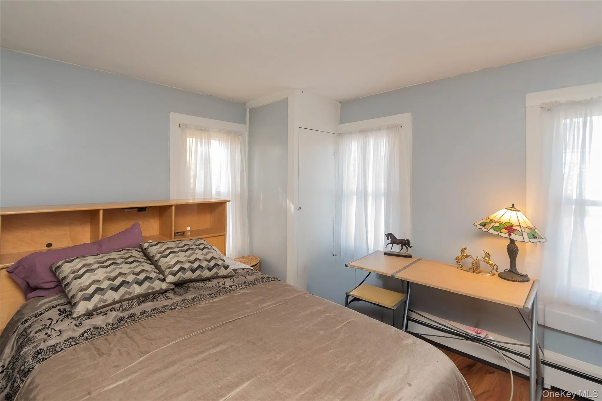 Bedroom with wood finished floors, multiple windows, and a baseboard radiator Bedroom with wood finished floors, multiple windows, and a baseboard radiator