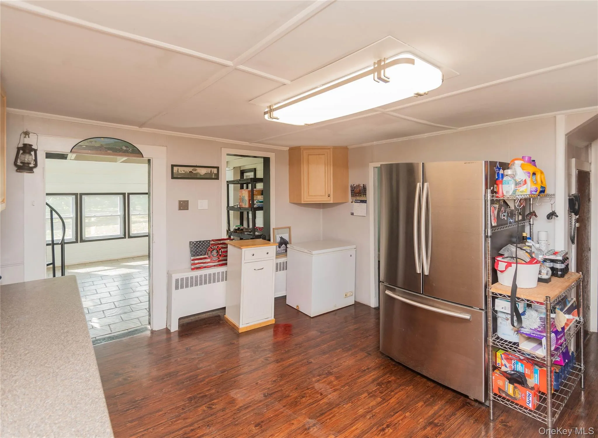 Kitchen featuring light countertops, radiator, dark wood finished floors, freestanding refrigerator, and light brown cabinets Kitchen featuring light countertops, radiator, dark wood finished floors, freestanding refrigerator, and light brown cabinets