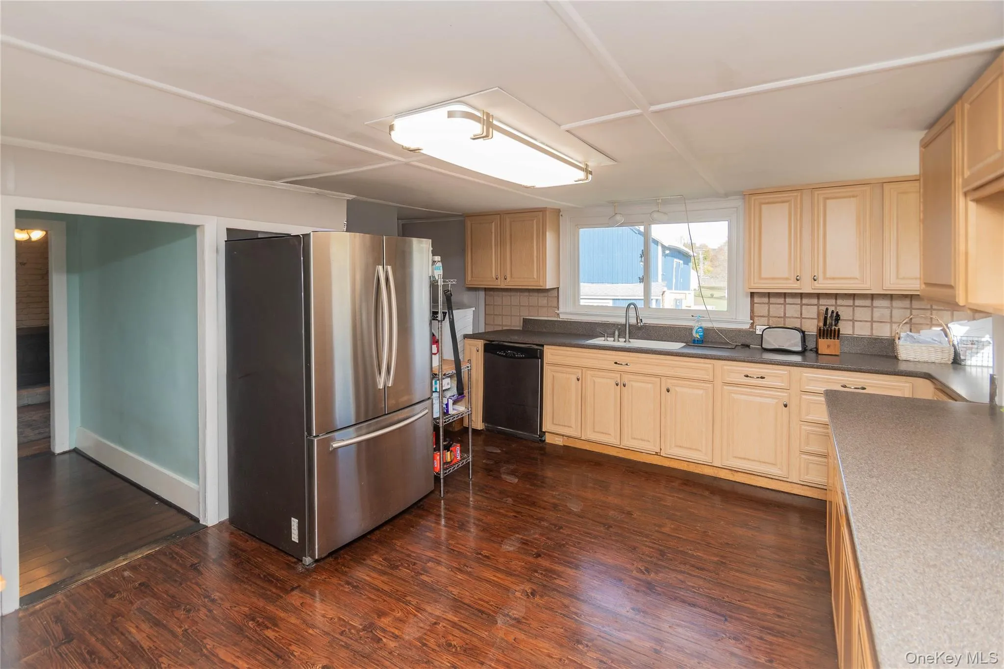 Kitchen with freestanding refrigerator, dark wood-type flooring, decorative backsplash, dark countertops, and black dishwasher Kitchen with freestanding refrigerator, dark wood-type flooring, decorative backsplash, dark countertops, and black dishwasher