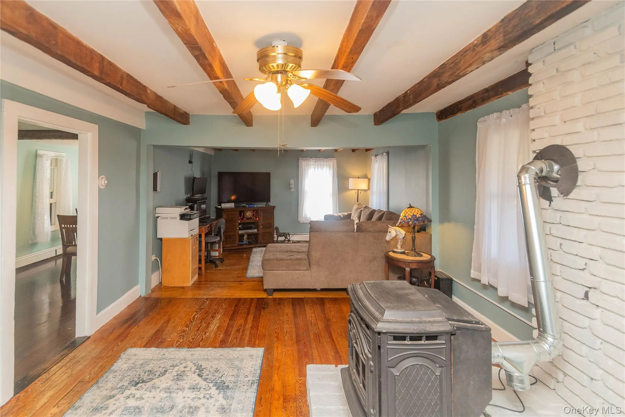 Living area featuring wood finished floors, beamed ceiling, a ceiling fan, and a wood stove Living area featuring wood finished floors, beamed ceiling, a ceiling fan, and a wood stove
