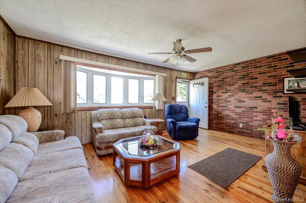 Hardwood flooring, bay window, wood paneling, exposed brick wall, and a ceiling fan with integrated lighting Hardwood flooring, bay window, wood paneling, exposed brick wall, and a ceiling fan with integrated lighting