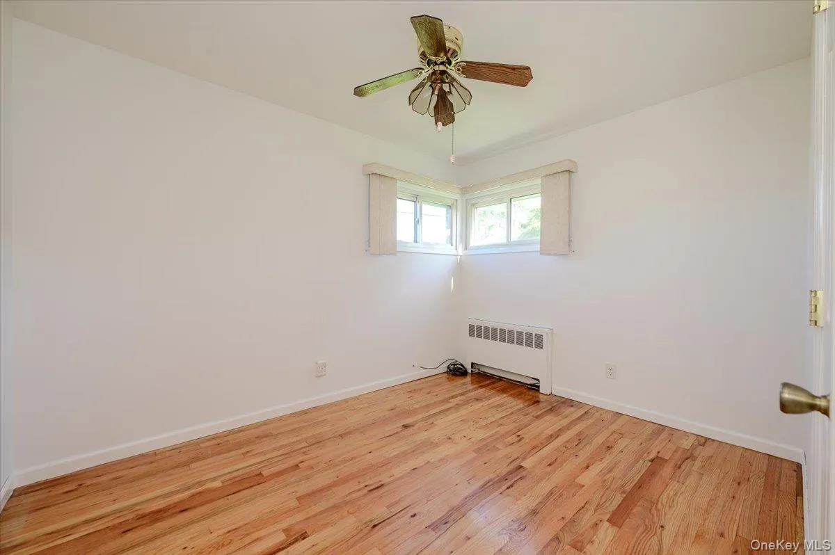 Natural wood flooring, white walls, two windows, radiator, and a ceiling fan with light fixture Natural wood flooring, white walls, two windows, radiator, and a ceiling fan with light fixture