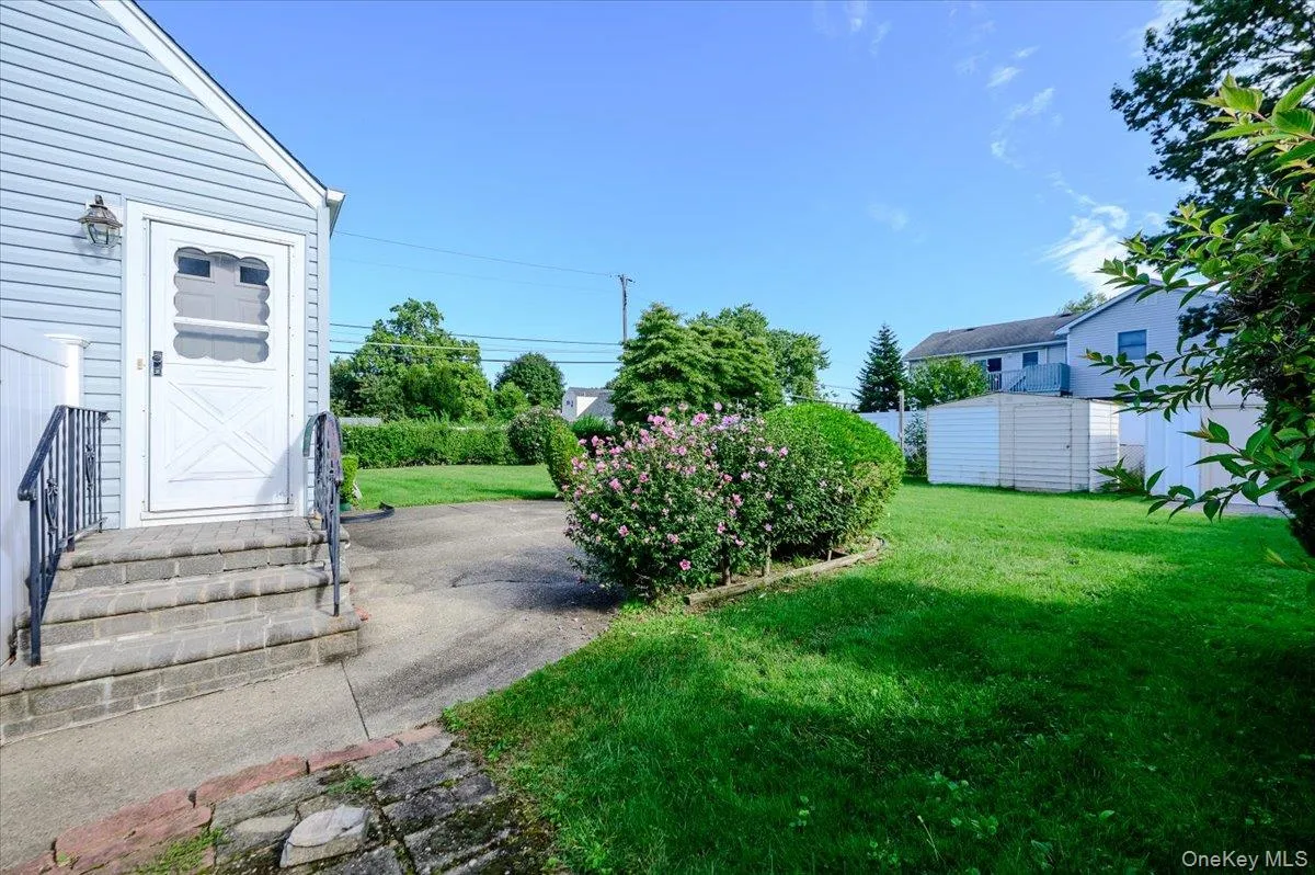 Light blue siding exterior with a white storm door, concrete steps with wrought iron railings, mature landscaping, and a detached storage shed Light blue siding exterior with a white storm door, concrete steps with wrought iron railings, mature landscaping, and a detached storage shed