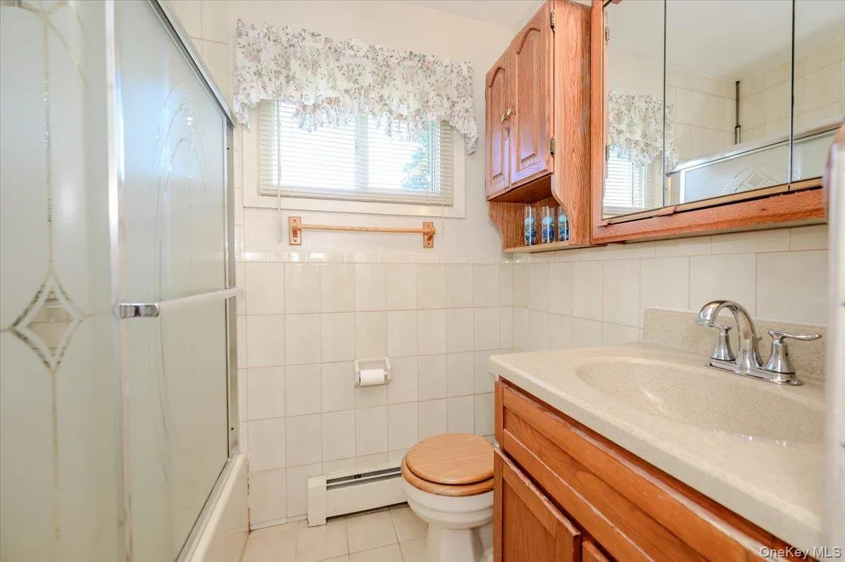 Bathroom featuring a wood-finish vanity with an integrated sink, a mirrored medicine cabinet, a full-size tub with a sliding glass enclosure, and tiled walls Bathroom featuring a wood-finish vanity with an integrated sink, a mirrored medicine cabinet, a full-size tub with a sliding glass enclosure, and tiled walls