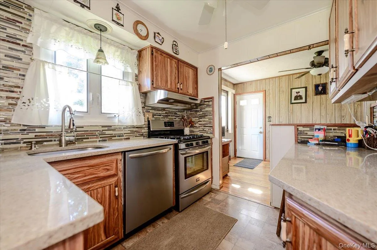 Kitchen with stainless steel appliances, wood-finish cabinetry, light-toned countertops, and a full tile backsplash Kitchen with stainless steel appliances, wood-finish cabinetry, light-toned countertops, and a full tile backsplash