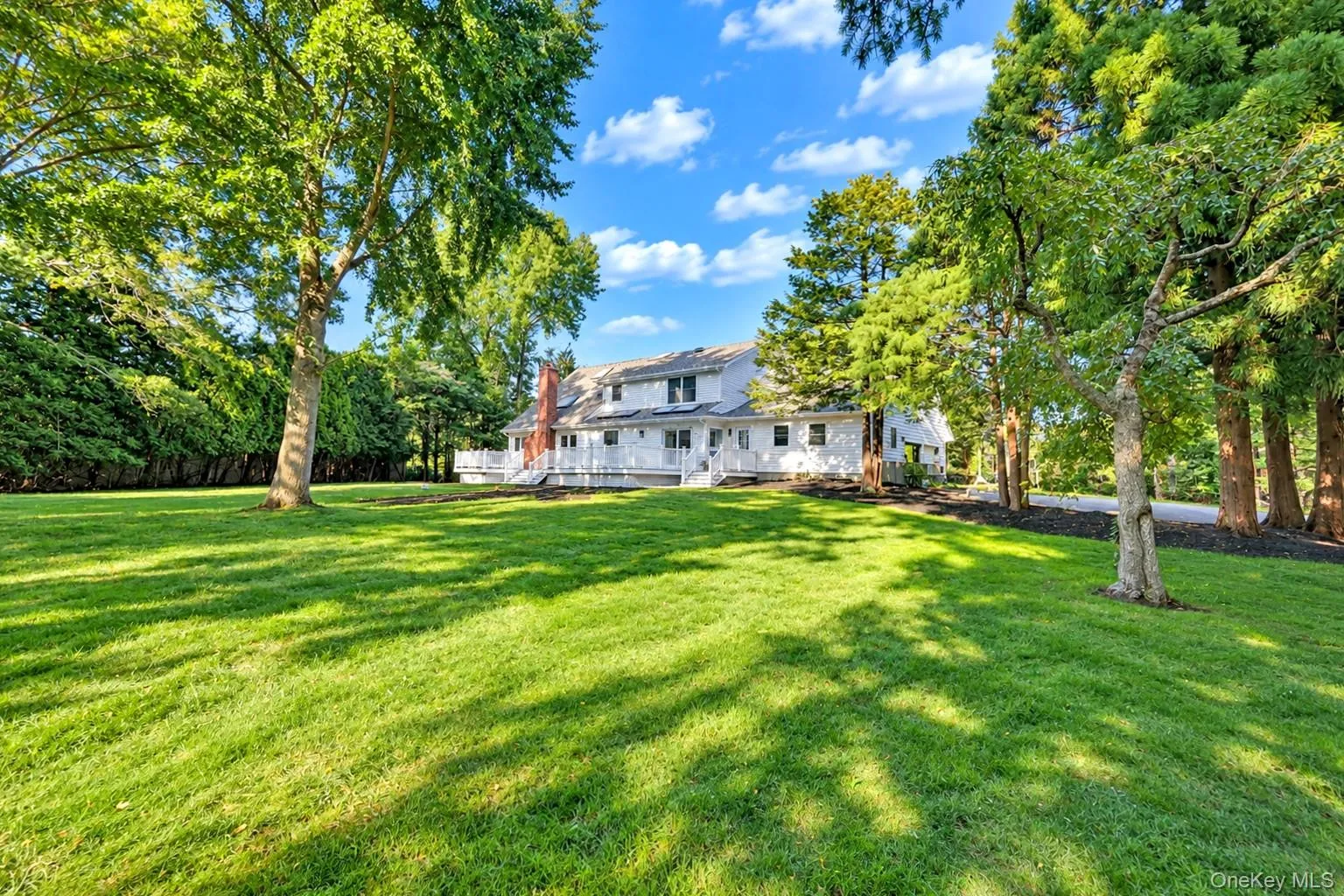 Expansive lawn with mature trees and a white multi-story residence featuring a deck and a brick chimney Expansive lawn with mature trees and a white multi-story residence featuring a deck and a brick chimney