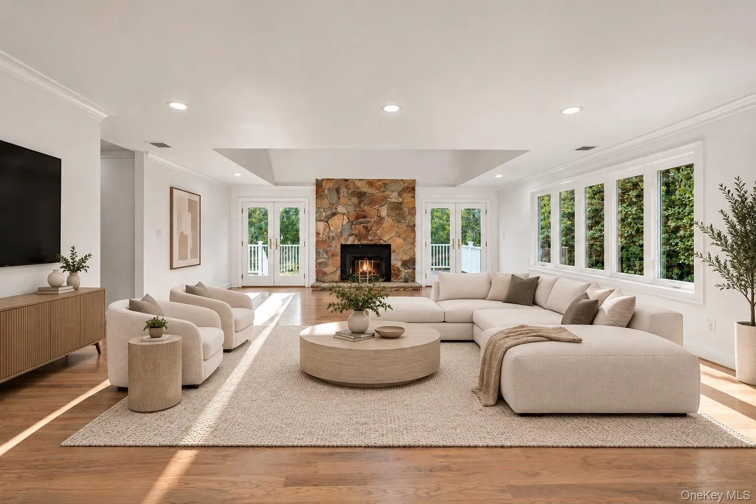 Spacious room featuring wood-finish flooring, a stone fireplace, and recessed lighting Spacious room featuring wood-finish flooring, a stone fireplace, and recessed lighting