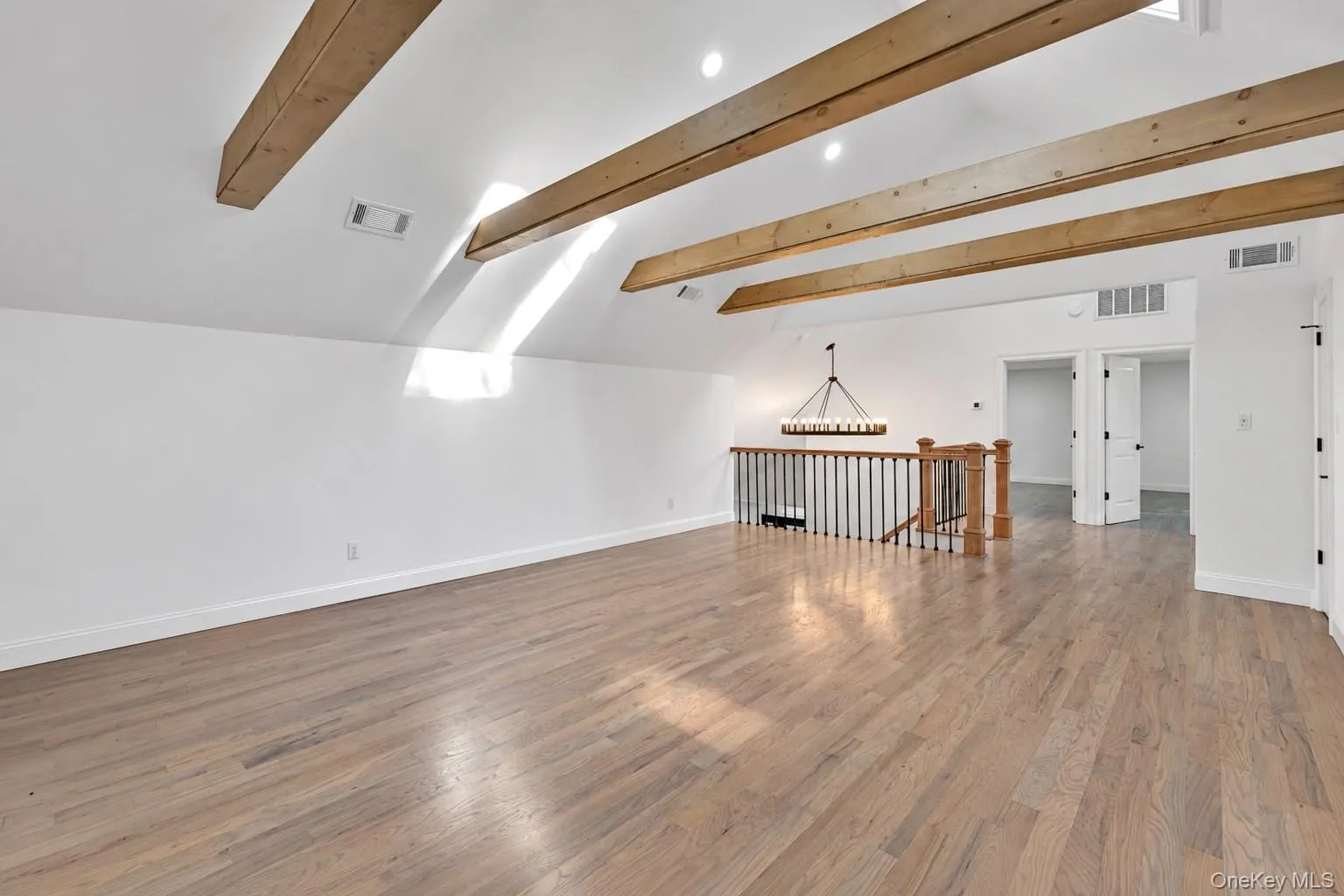 High vaulted ceiling with exposed wood beams, wood-finish flooring, staircase with wrought iron balusters and wood newel posts, and recessed lighting High vaulted ceiling with exposed wood beams, wood-finish flooring, staircase with wrought iron balusters and wood newel posts, and recessed lighting